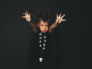 little boy with red halloween horns and black cape in front of black background