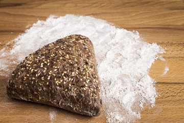 Triangle-shaped wholemeal bread with linseed, oats and sesame seeds next to some ingredients on a wooden table
