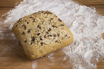 Bread with linseed, oats and sesame seeds next to some ingredients on a wooden table
