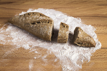 small loaf of whole wheat bread elongated on flour on a wooden table
