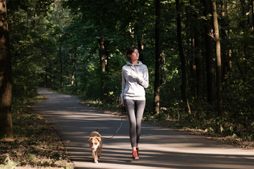 Woman jogging with dog in beautiful forest. Young female person with pet doing cross country running excercise in fresh air.