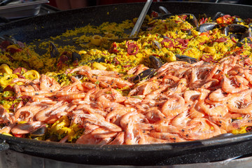 Street food in France, fresh prepared paella with rice and sea food in big pan on street market, ready to eat