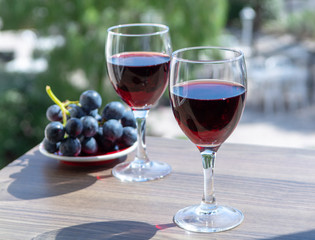 Two wine glasses with red wine served with red grape on outdoor terrace