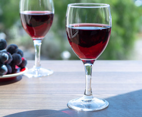 Two wine glasses with red wine served with red grape on outdoor terrace