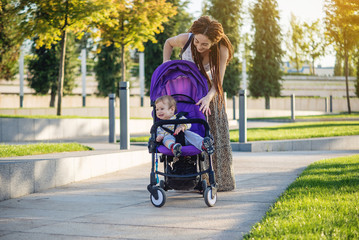 Young modern mother with baby son in stroller walking in Sunny Park. Concept of the joy of motherhood and autumn mood