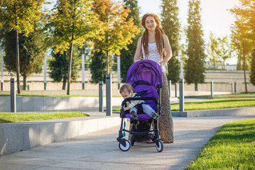 Young modern mother with baby son in stroller walking in Sunny Park. Concept of the joy of motherhood and autumn mood