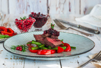 Sliced venison steak with lingonberry sauce, roast red peppers and green beans