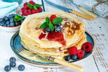 A stack of pancakes with fresh fruit, jam and cream on a plate