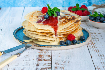 A stack of pancakes with fresh fruit, jam and cream on a plate