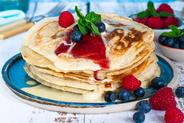 A stack of pancakes with fresh fruit, jam and cream on a plate