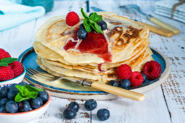 A stack of pancakes with fresh fruit, jam and cream on a plate