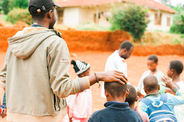 Fototapeta na wymiar Bafoussam, Cameroon - 06 august 2018: young african teacher caress school boy while playing outside village school
