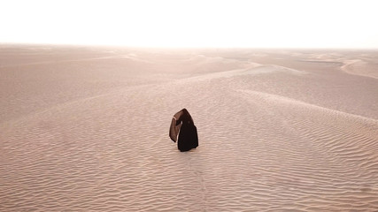 A woman in abaya (United Arab Emirates traditional dress) walking on the dunes in the desert during...
