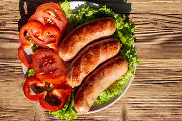 Grilled sausages with fresh vegetables on wooden table