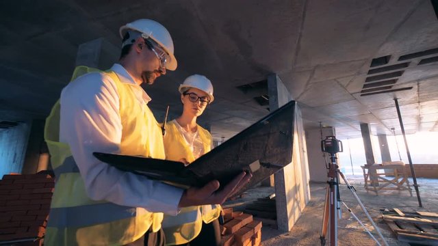 Construction site with two builders, constructors walking with layouts and a laptop and talking