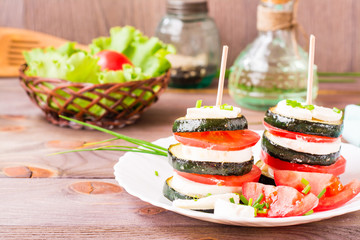 Original appetizer from fried zucchini, fresh tomatoes and feta cheese on a wooden skewer on a plate. Copy space