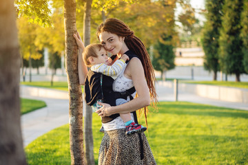 Young modern happy mom with baby son walking in Sunny Park. The concept of the joy of motherhood