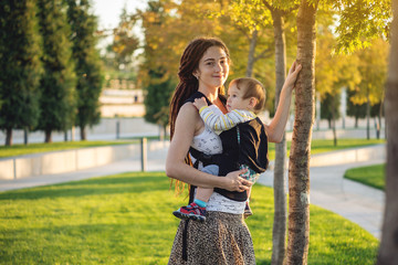 Young modern happy mom with baby son walking in Sunny Park. The concept of the joy of motherhood