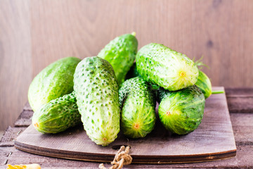 A few fresh ripe cucumbers on cutting board on a wooden table. Rustic style