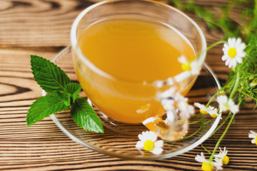 Full glass cup of green tea and mint and bunch of chamomile on old wooden table. Healthy concept
