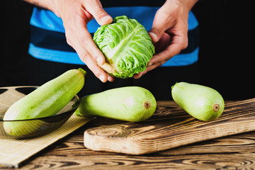 Man holds fresh cabbage on old brown wooden table with kitchenware on black background
