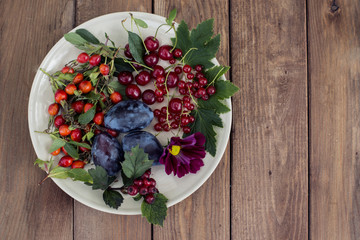 Ceramic dish  with berries and plums on a wooden background.