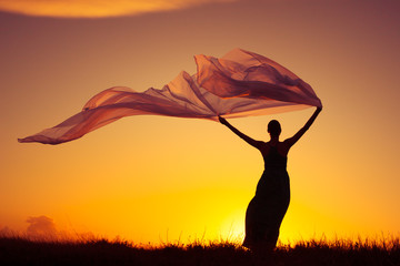 Woman outdoors wearing dress holding a long fabric blowing in the wind. Freedom and serenity...