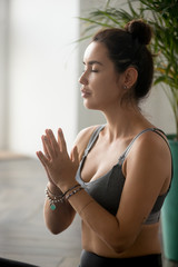 Portrait of young attractive yoga woman, doing meditation exercise, relaxation pose with namaste, working out, wearing sportswear, indoor close up, at yoga studio. Hobby wellbeing activity concept
