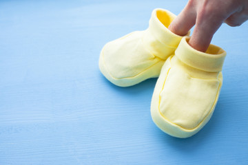Baby yellow booties. Children's shoes in women hands and toys on blue background. Newborn.