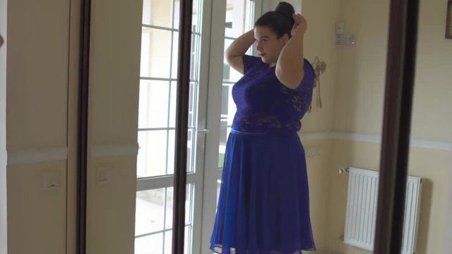 Fat girl in a blue dress in front of a mirror