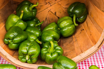 Bunch of green bell peppers in a basket on it's side. Red and white checkered tablecloth