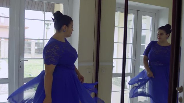 Fat girl in a blue dress in front of a mirror