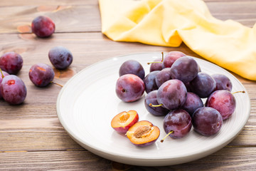 Ripe blue plum on a plate on a wooden table