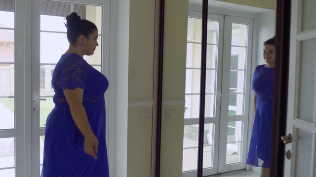 Fat girl in a blue dress in front of a mirror