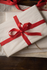 Preparation of christmas gifts. Present covered in white paper with red ribbon. Overhead view.