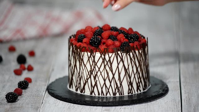 Pastry chef decorates a cake with berries.