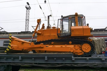 heavy orange bulldozer stands on the flatcar of the train for accident recovery work
