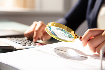 Businesswoman Examining Invoice Through Magnifying Glass