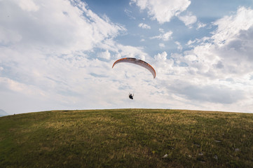 A white-orange paraglider flies over the mountainous terrain
