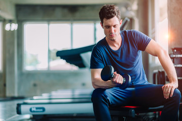 Fototapeta na wymiar Fit caucasian handsome young man and big muscle in sportswear. Young man holding dumbbell during an exercise class in a gym. Healthy sports lifestyle, Fitness concept. with copy space for your text.