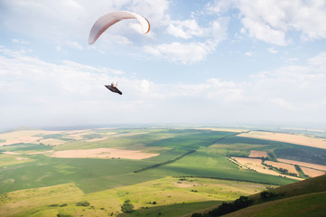 A white-orange paraglider flies over the mountainous terrain