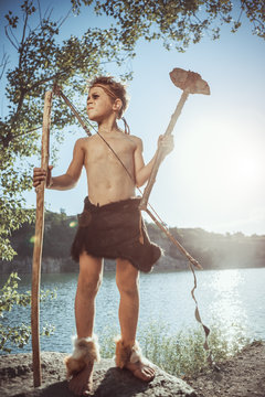 Caveman, manly man with stone axe and bow hunting near river. Prehistoric tribal boy outdoors on nature. Young shaggy and dirty savage, warrior and hunter. Primitive ice age man in animal skin