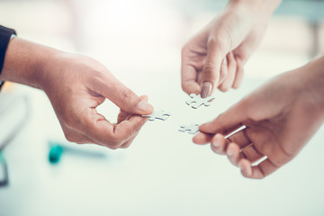 Business teamwork, partnership and brainstorm concept. Group of business people assembling jigsaw puzzle pieces together on desk table.