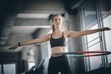Fototapeta na wymiar Beautiful caucasian young woman doing hula hoop in step waist hooping forward stance. Young woman doing hula hoop during an exercise class in a gym. Healthy sports lifestyle, Fitness, Healthy concept.