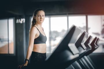 Fototapeta na wymiar Fit young woman caucasian running on machine treadmill workout in gym. Glad smiling girl is enjoy with her training process. Concept of fitness, healthy life, Sport, Lifestyle.