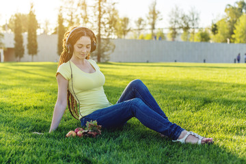 Fototapeta premium Beautiful modern girl listening to music with her headphones in autumn Sunny Park. Favorite music, happy time.