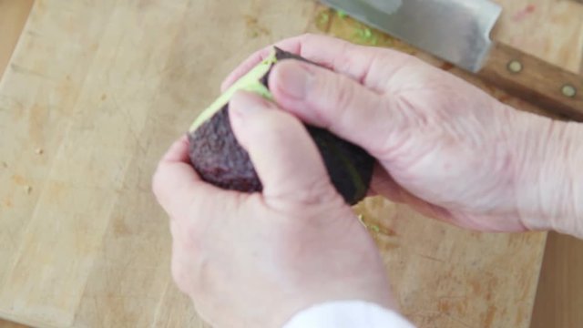 A woman removes peel from an avocado over a cutting board