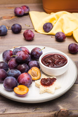 Appetizing bruschetta from fresh bread with plum jam and ripe berries of blue plums on a plate on a wooden table