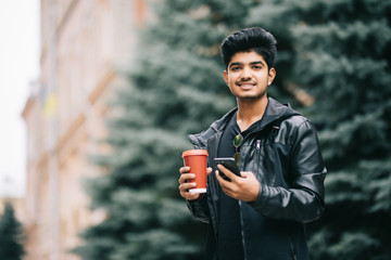 Young Indian man student texting on smartphone in the city street