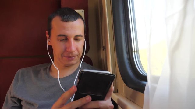 man listening to the music on the train rail car coupe compartment travel. slow motion video. man with a smartphone at the window of a train in a car travel lifestyle internet social media web. man
